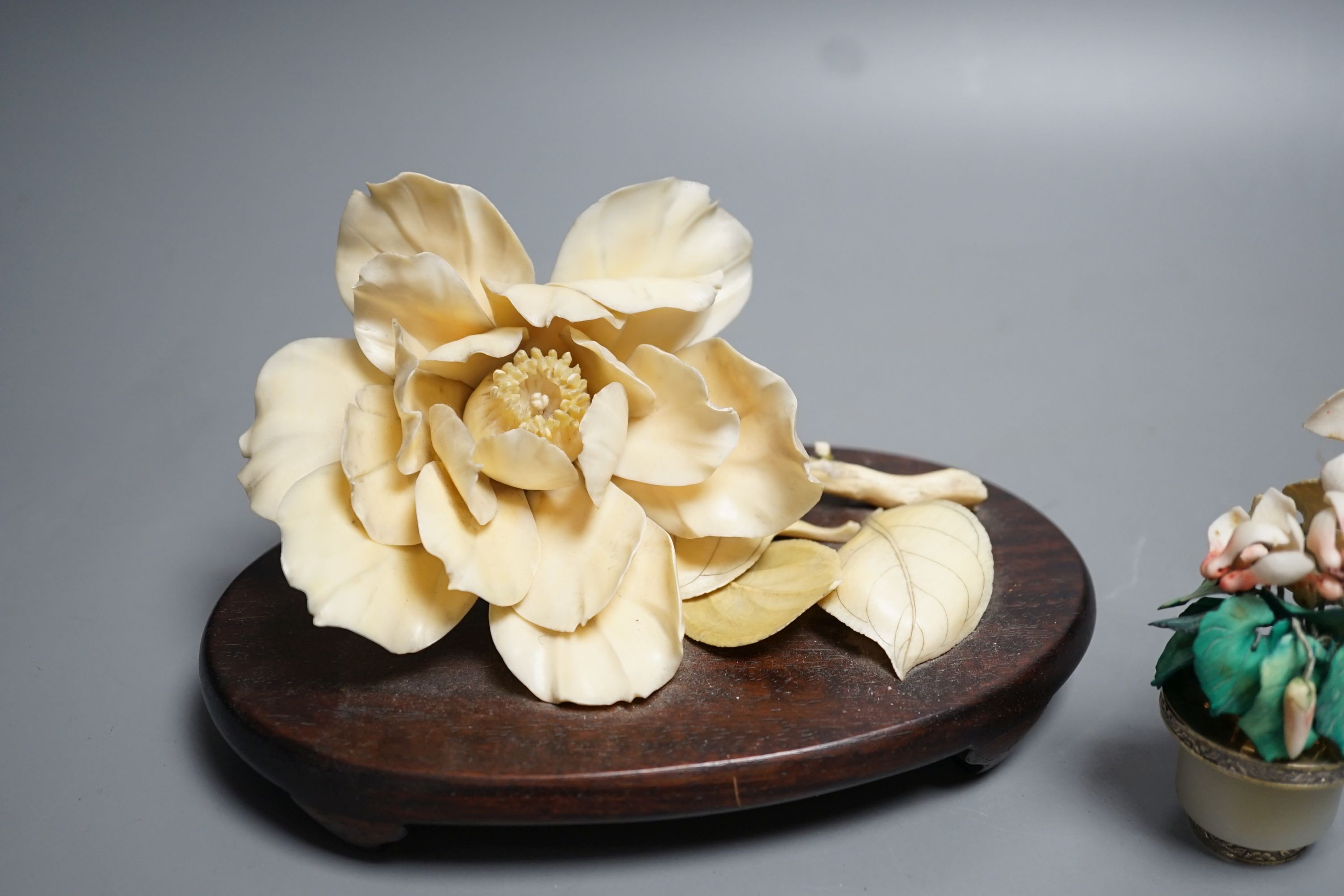 A Chinese ivory model of a peony flower on stand and a Chinese coloured ivory model of flowers with a white jade and white metal plant pot, first half 20th century. Largest measurement 19cm